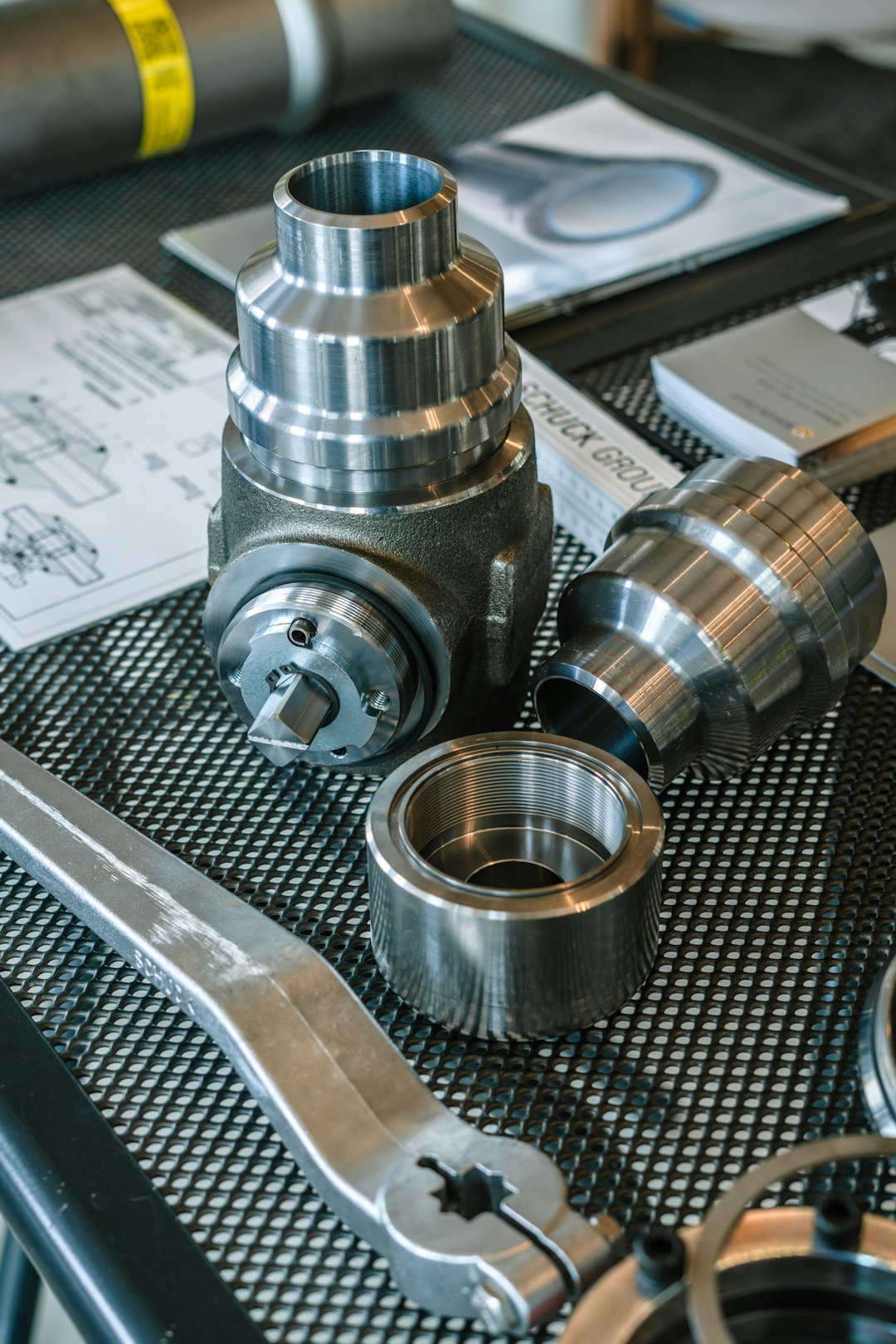 various-metal-mechanical-parts-and-blueprints-on-a-mesh-table-.jpg Diversas peças mecânicas de metal e plantas sobre uma mesa de malha.